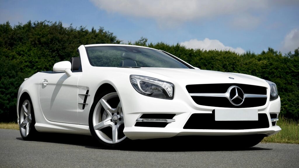 Stunning white Mercedes Benz convertible parked on the road against a lush green backdrop.