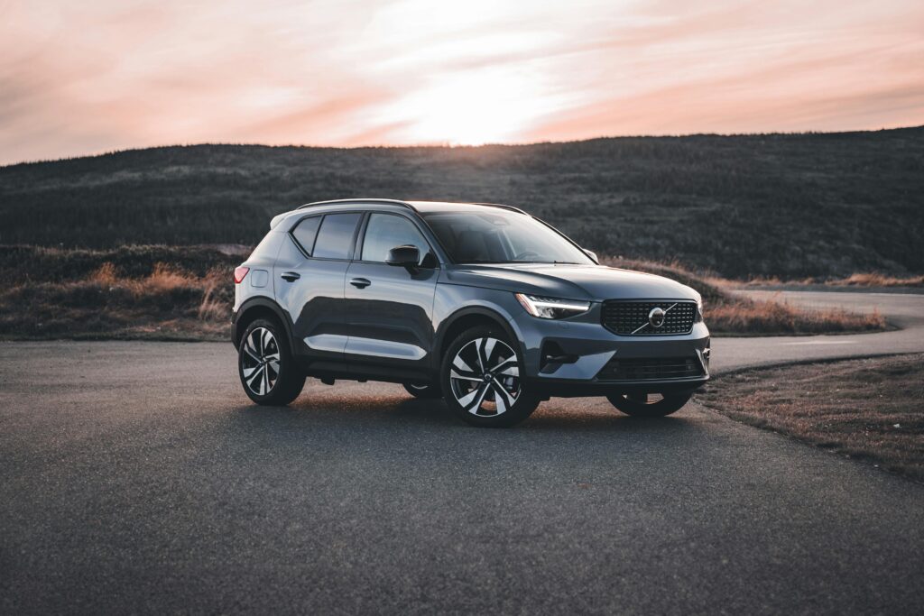 A Volvo SUV parked on a scenic road at sunrise, surrounded by hills.